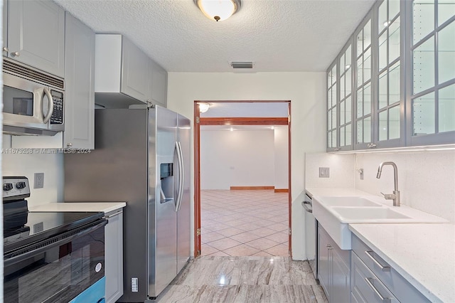 kitchen featuring gray cabinetry, stainless steel appliances, sink, light tile patterned floors, and a textured ceiling