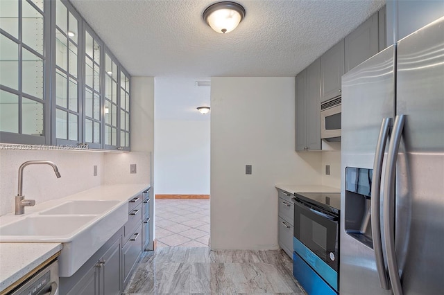 kitchen with sink, appliances with stainless steel finishes, gray cabinetry, and a textured ceiling