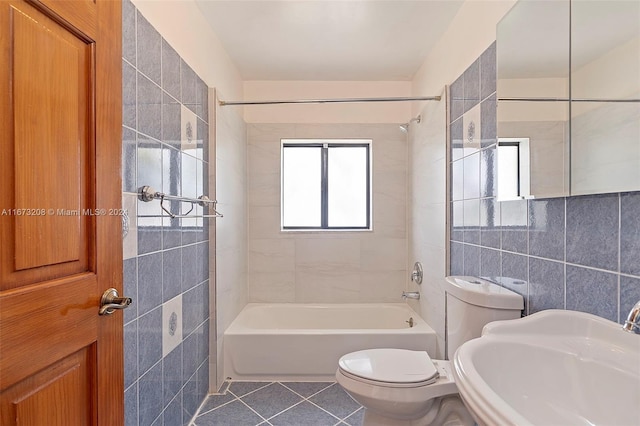 full bathroom featuring toilet, tile patterned flooring, sink, tiled shower / bath combo, and tile walls