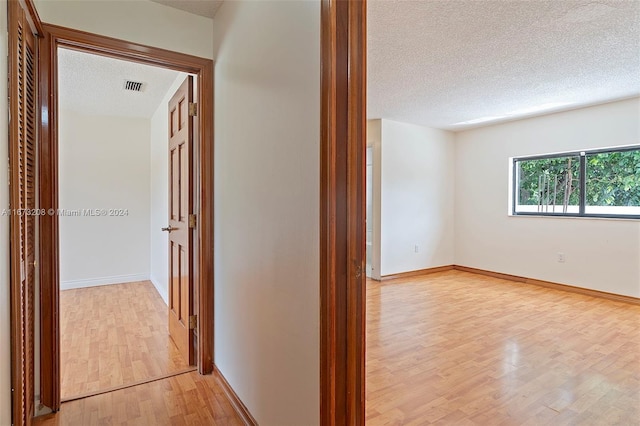 hallway with light hardwood / wood-style flooring and a textured ceiling