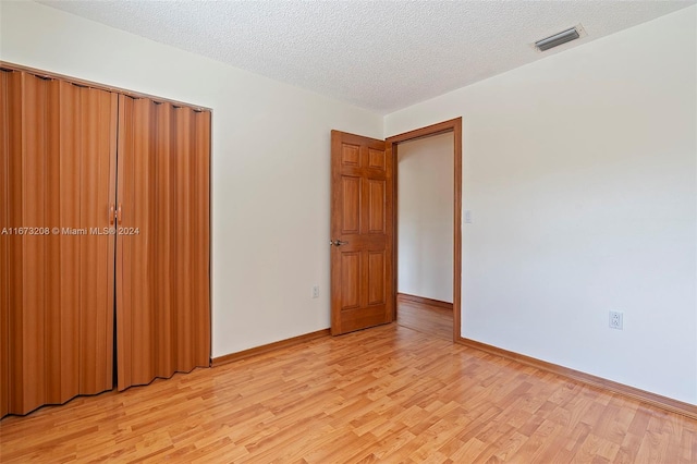 unfurnished bedroom featuring a closet, a textured ceiling, and light hardwood / wood-style flooring