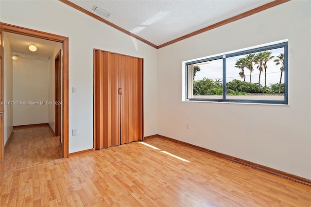 unfurnished bedroom with lofted ceiling, a closet, light hardwood / wood-style flooring, crown molding, and a textured ceiling