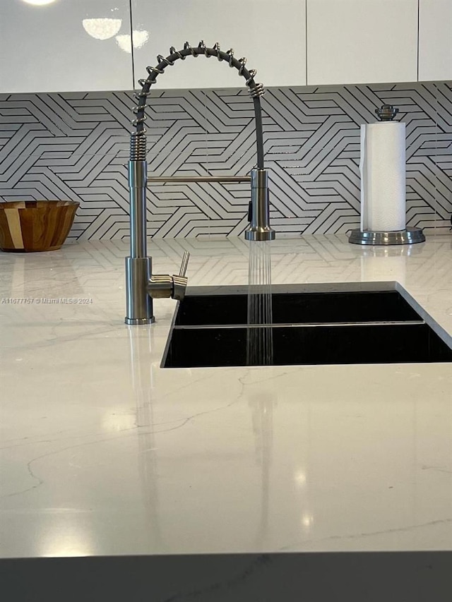 interior details featuring light stone counters, white cabinetry, and sink