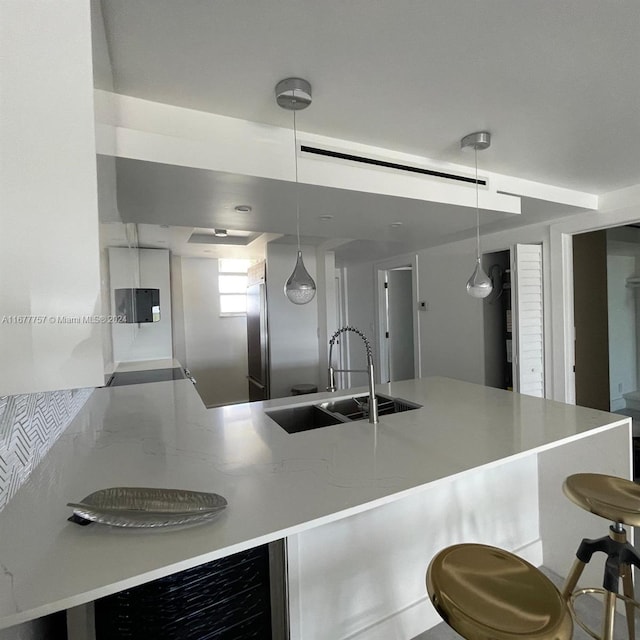 kitchen with stainless steel built in fridge, sink, decorative backsplash, decorative light fixtures, and a breakfast bar area