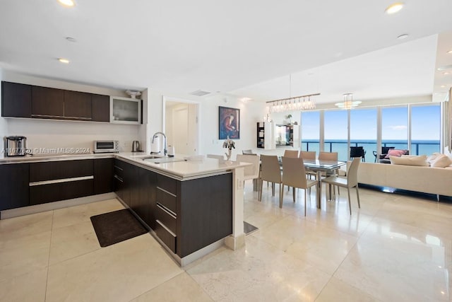 kitchen with kitchen peninsula, dark brown cabinets, sink, a notable chandelier, and a water view