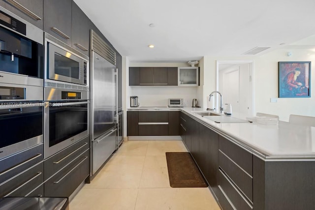 kitchen with built in appliances, light tile patterned floors, kitchen peninsula, and sink