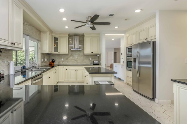 kitchen with cream cabinets, ceiling fan, appliances with stainless steel finishes, wall chimney exhaust hood, and sink