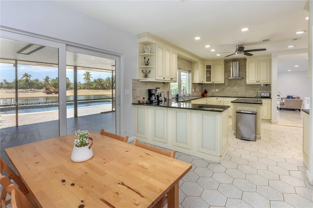 kitchen featuring tasteful backsplash, wall chimney range hood, sink, cream cabinetry, and ceiling fan