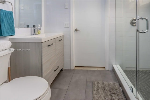 bathroom with tile patterned floors, toilet, vanity, tile walls, and an enclosed shower