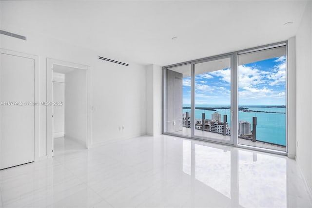 unfurnished room featuring a wall of windows, a water view, visible vents, and baseboards