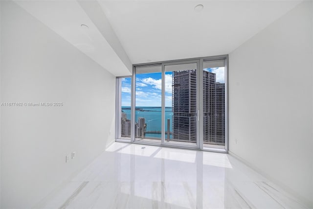 empty room with floor to ceiling windows, a water view, and baseboards