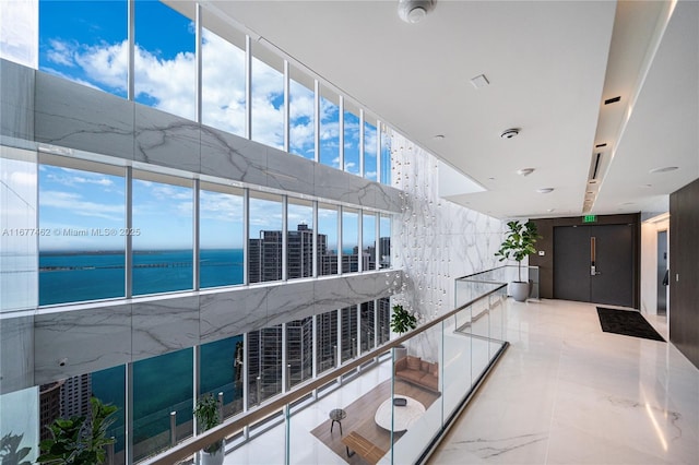 corridor featuring a water view, marble finish floor, and tile walls