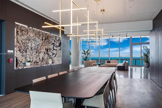 dining room featuring a water view, a wall of windows, a notable chandelier, and wood finished floors