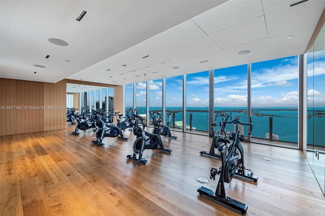 workout area featuring a water view, wooden walls, expansive windows, and hardwood / wood-style floors