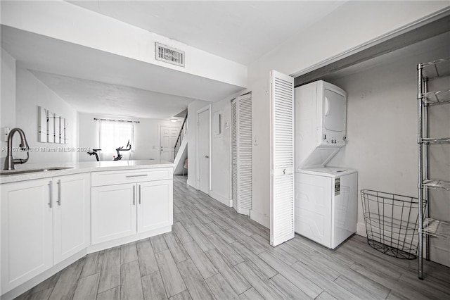 laundry room featuring sink, stacked washer and dryer, and light hardwood / wood-style floors