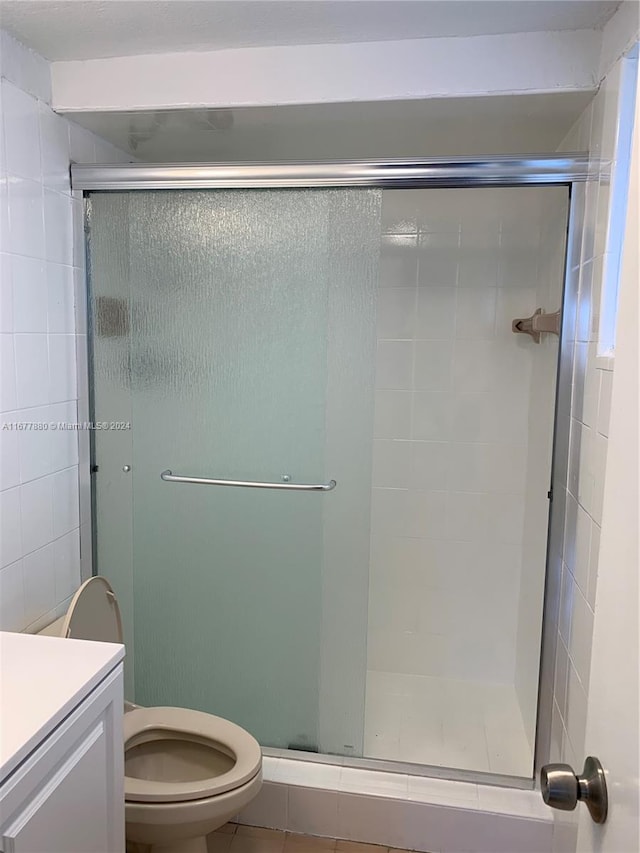 bathroom with a shower with door, vanity, toilet, and tile patterned floors