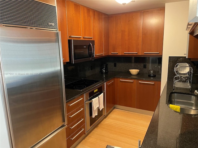 kitchen with decorative backsplash, dark stone counters, sink, appliances with stainless steel finishes, and light hardwood / wood-style floors