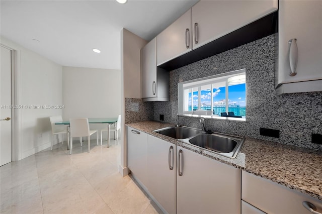 kitchen featuring backsplash, light stone countertops, sink, and light tile patterned floors