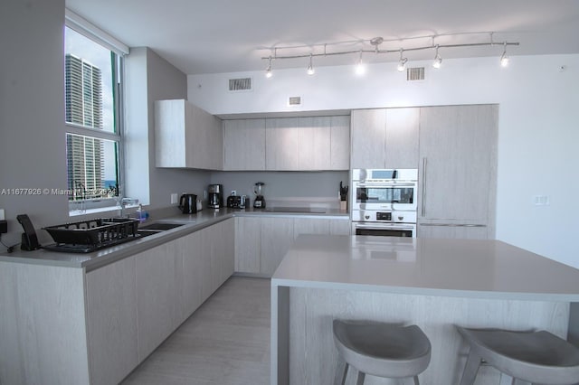 kitchen featuring a kitchen breakfast bar, black electric cooktop, light wood-type flooring, and stainless steel double oven