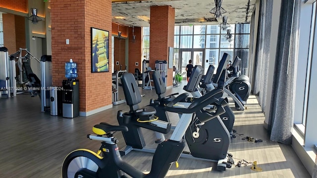 exercise room featuring hardwood / wood-style flooring, brick wall, and floor to ceiling windows