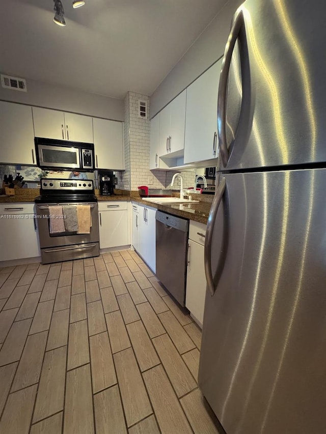 kitchen featuring appliances with stainless steel finishes, light hardwood / wood-style flooring, white cabinetry, and decorative backsplash