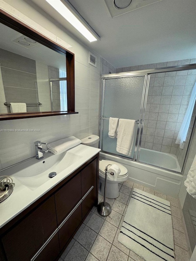 full bathroom featuring vanity, toilet, combined bath / shower with glass door, and tile walls