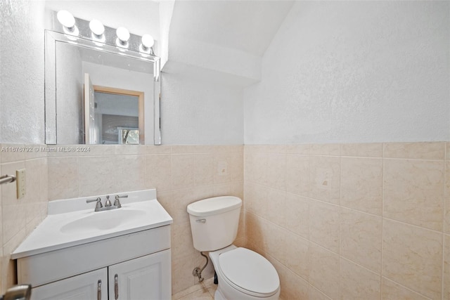 bathroom with tile walls, vanity, lofted ceiling, and toilet