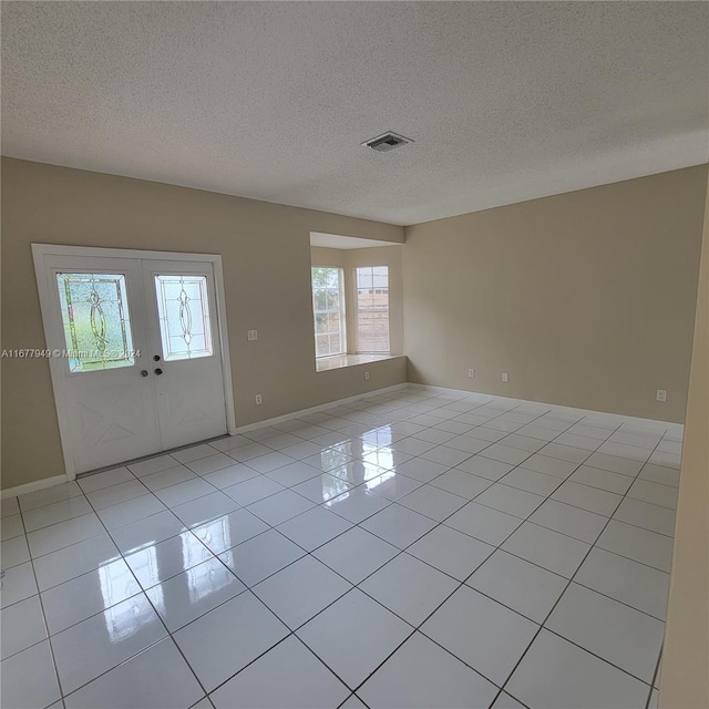 tiled empty room with a textured ceiling and french doors