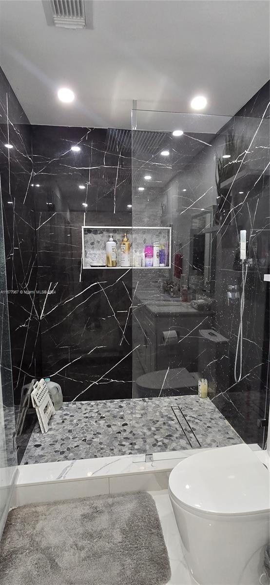 bathroom with a tile shower, toilet, and tile walls