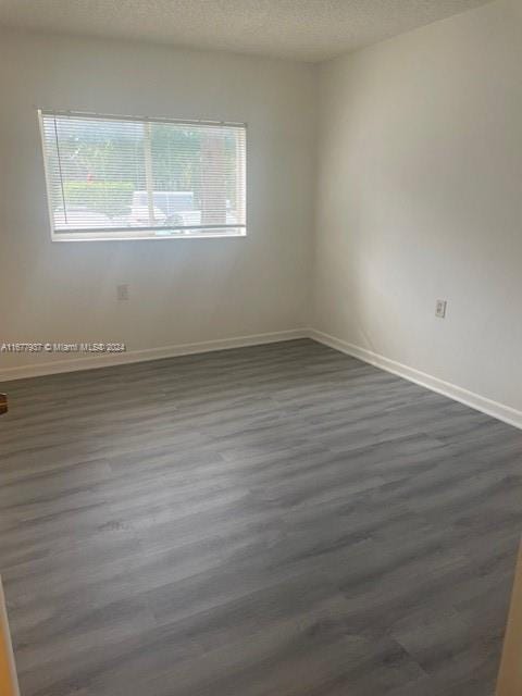 1068NBENOIST Farm Rd Unit 105, West Palm Beach, FL 33411 - spare room featuring dark wood-type flooring, baseboards, and a textured ceiling