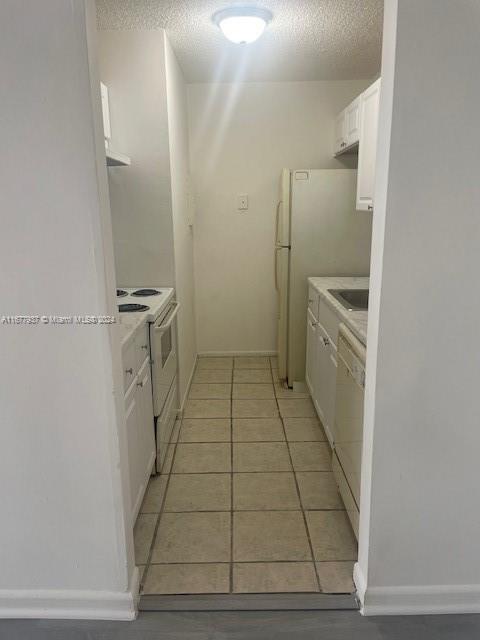 1068NBENOIST Farm Rd Unit 105, West Palm Beach, FL 33411 - kitchen featuring white appliances, white cabinets, light countertops, light tile patterned floors, and a textured ceiling
