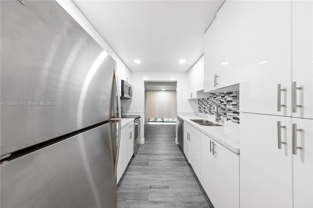 kitchen with decorative backsplash, white cabinets, wood-type flooring, sink, and stainless steel appliances