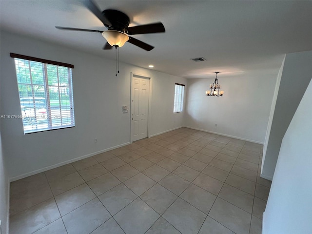 tiled spare room featuring ceiling fan with notable chandelier