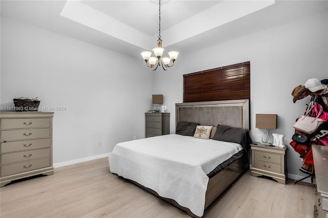 bedroom featuring a chandelier, a tray ceiling, and light wood-type flooring