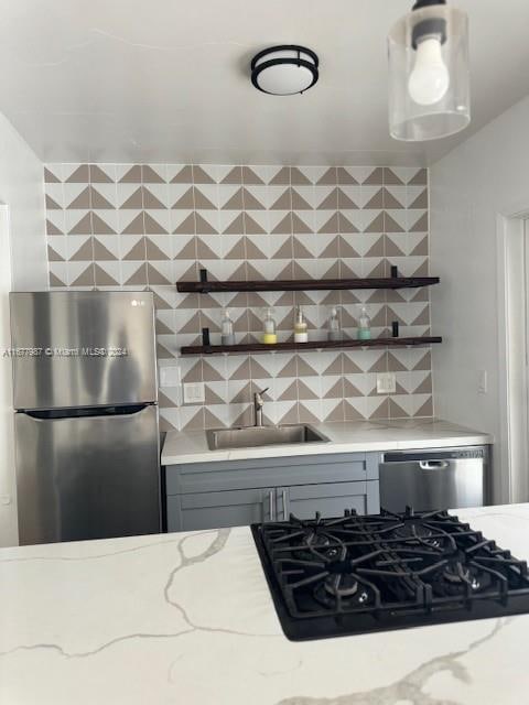 kitchen with appliances with stainless steel finishes, decorative backsplash, light stone countertops, and sink