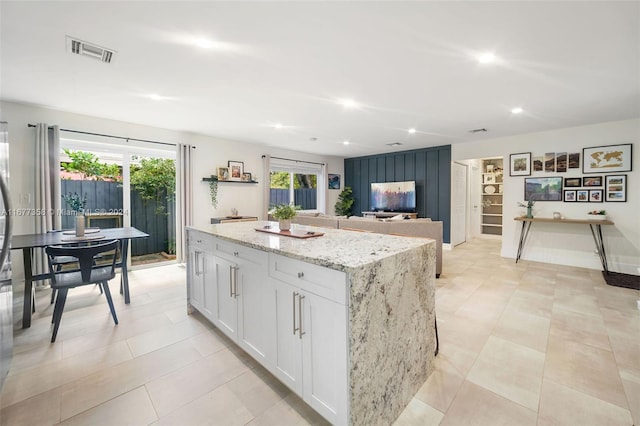 kitchen with a center island, light stone counters, plenty of natural light, and white cabinets