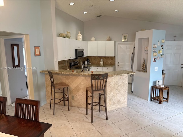 kitchen with kitchen peninsula, appliances with stainless steel finishes, a kitchen breakfast bar, white cabinetry, and light stone countertops