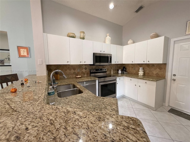 kitchen featuring stone counters, sink, kitchen peninsula, stainless steel appliances, and high vaulted ceiling