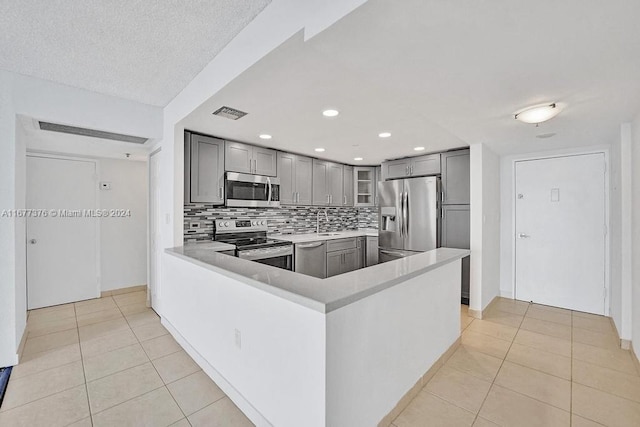 kitchen featuring tasteful backsplash, kitchen peninsula, stainless steel appliances, gray cabinets, and light tile patterned floors