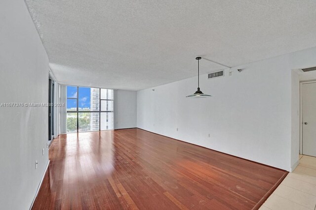 empty room with a textured ceiling, light wood-type flooring, and floor to ceiling windows