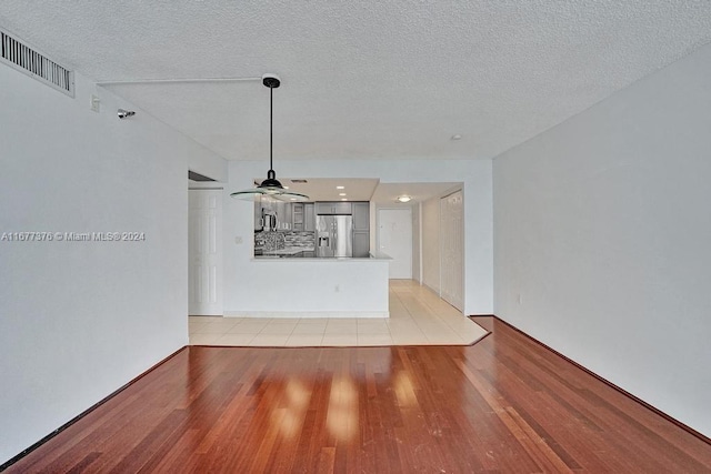 unfurnished living room featuring light hardwood / wood-style flooring, a textured ceiling, and ceiling fan