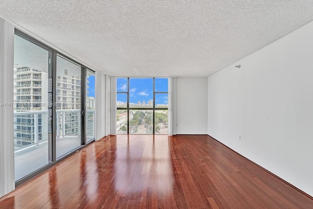 unfurnished room featuring a wall of windows, hardwood / wood-style flooring, and a textured ceiling