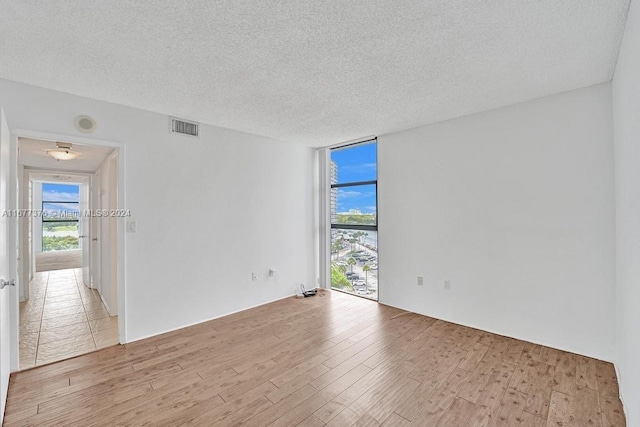 unfurnished room featuring a textured ceiling, light hardwood / wood-style flooring, and floor to ceiling windows