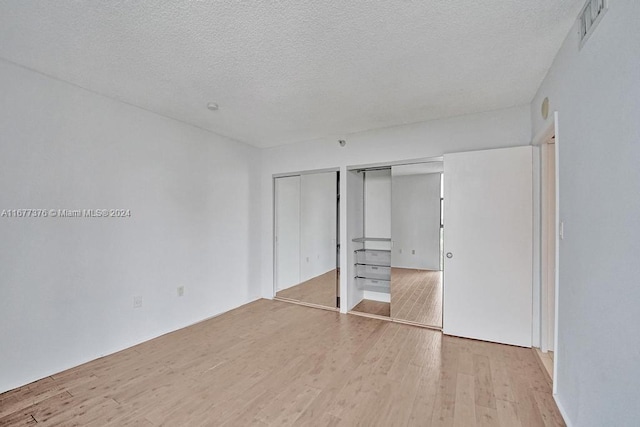 unfurnished bedroom featuring light hardwood / wood-style flooring, a textured ceiling, and two closets