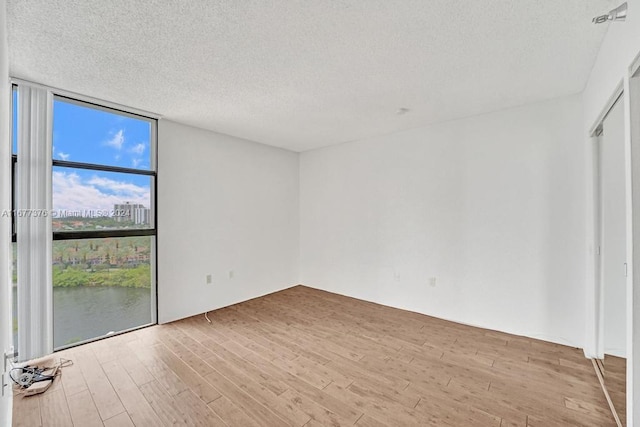 empty room with a textured ceiling, light hardwood / wood-style flooring, and floor to ceiling windows