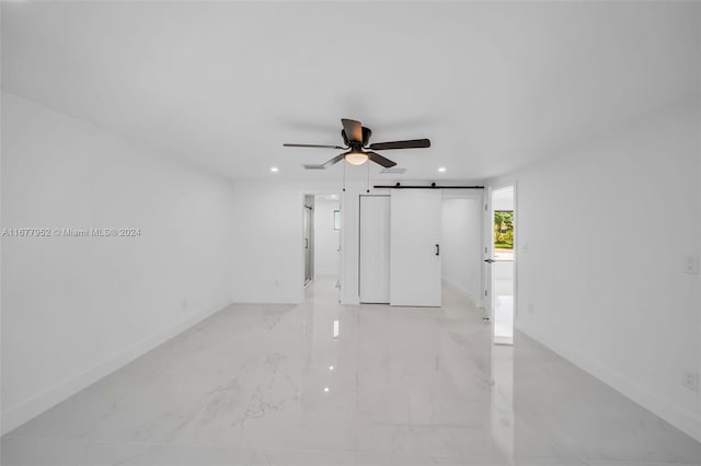 spare room with a barn door and ceiling fan