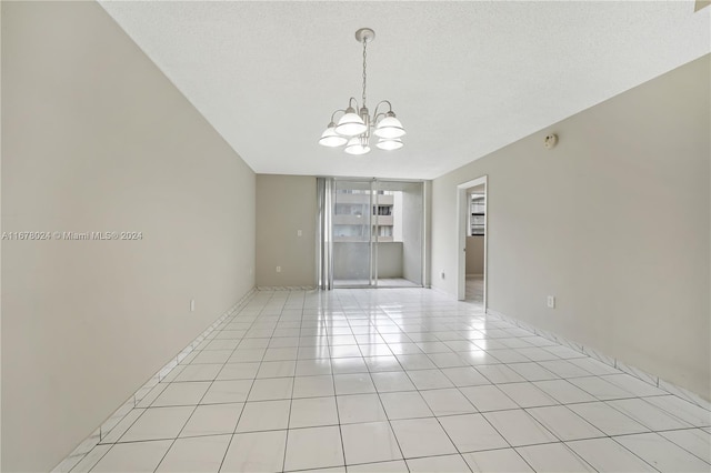 spare room with an inviting chandelier, a textured ceiling, and light tile patterned flooring