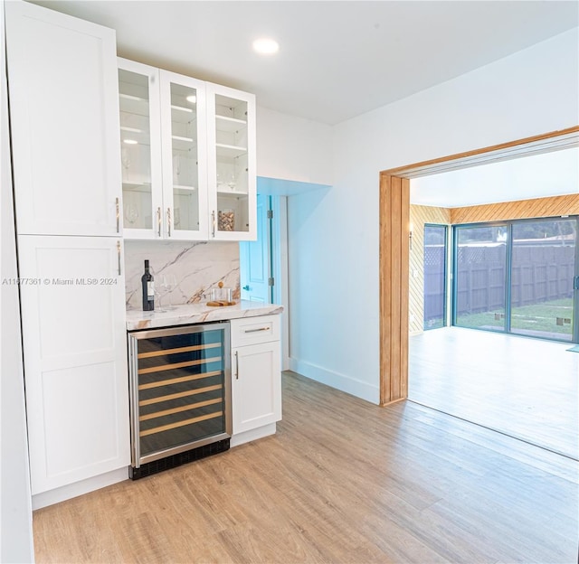 bar featuring backsplash, light hardwood / wood-style flooring, light stone counters, white cabinetry, and beverage cooler