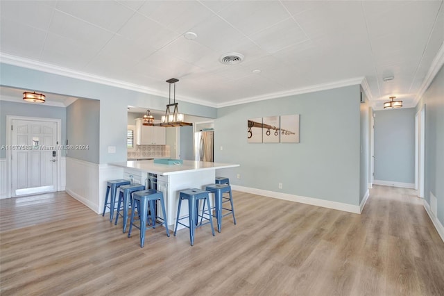 kitchen featuring kitchen peninsula, hanging light fixtures, white cabinetry, stainless steel refrigerator, and light hardwood / wood-style floors