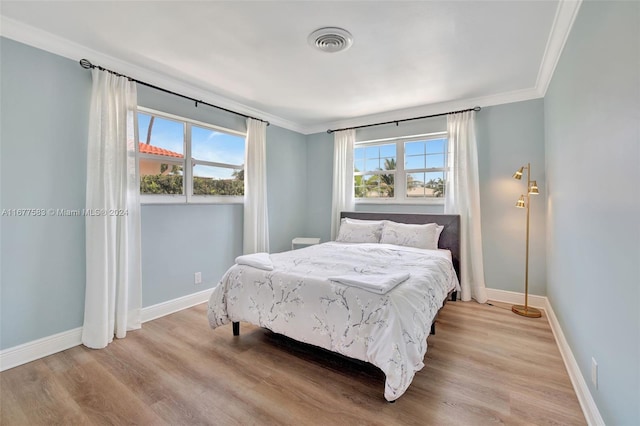 bedroom with ornamental molding, multiple windows, and light hardwood / wood-style floors